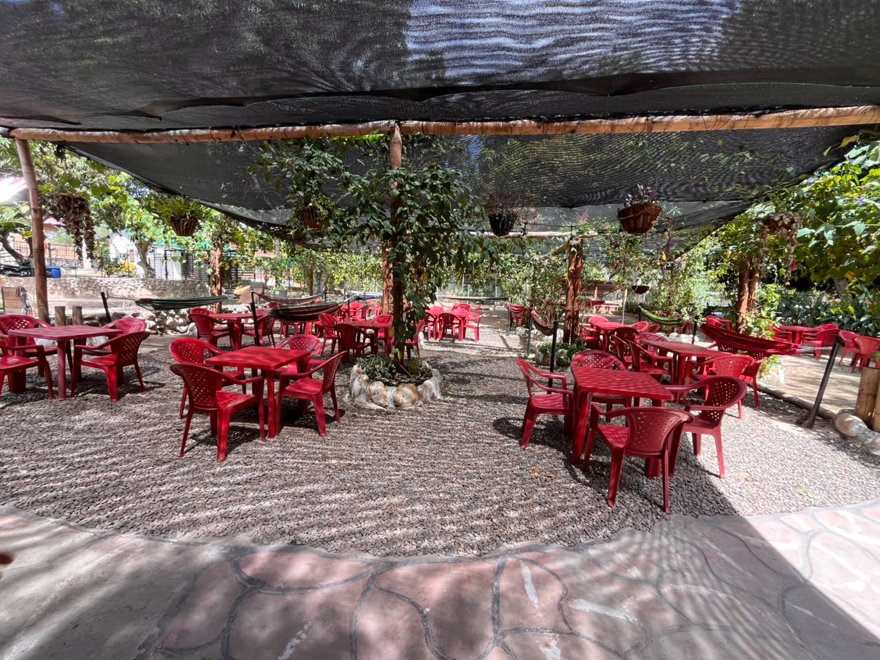 Zona de restaurante bajo sombra con mesas rojas